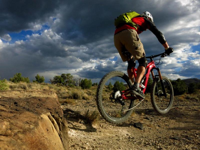 Rider jumping their bike off a ledge with a desert landscape and stormy sky. Photo by Anne Linger.