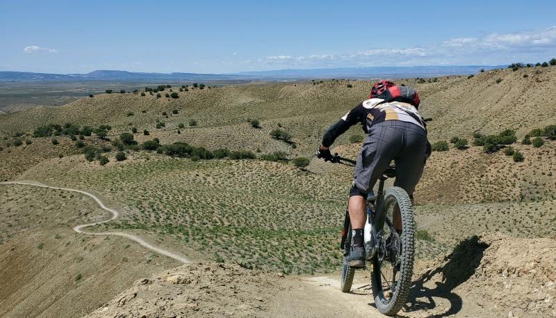 Rider going down knife edge trail, lots of desert and trail seen in the distance. Photo by Marc Huster.