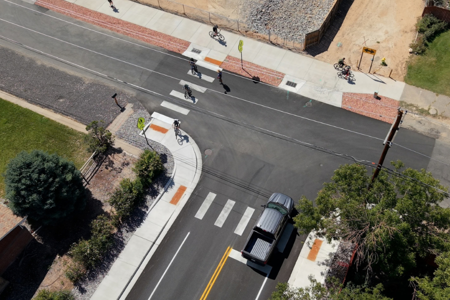 Drone photo of the intersection of Greenbelt Drive and 22 ½ Road. A line of bicycles goes through one of the crosswalks at the intersection while a truck waits at a stop sign.
