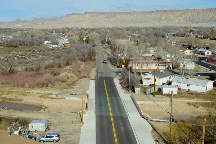 Drone photo of 32 ½ Road and the Grand Valley Canal. Houses and trees are in the foreground, and the Book Cliffs to the north are in the background.