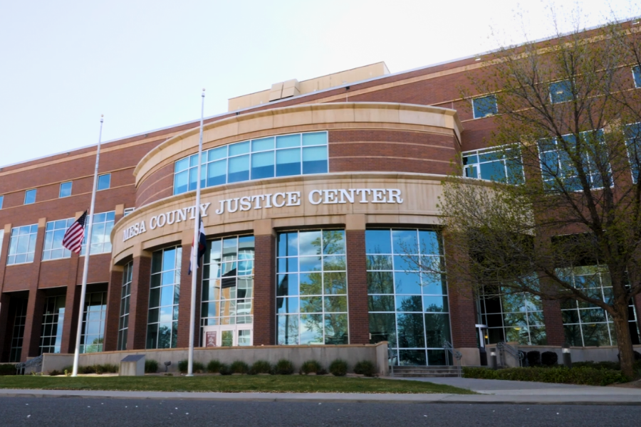 Low angle photo of the Mesa County Justice Center on Spruce Street. The road, lawn and flagpoles are in front of the large building.