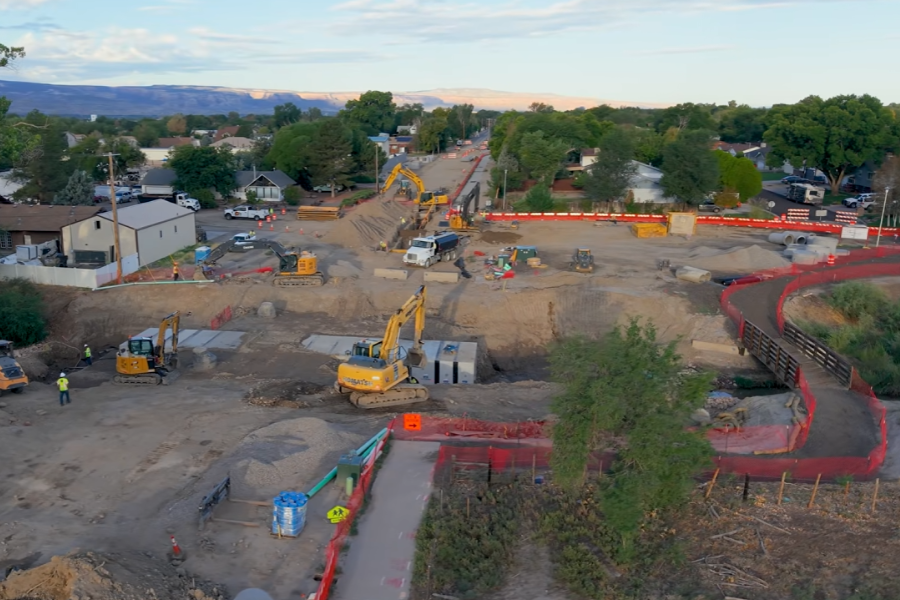 Drone photo of road construction near E ½ and 31 Road. Heavy machinery is operating near a wash to install the foundation for a bridge, with the area surrounded by dirt and orange construction barriers.